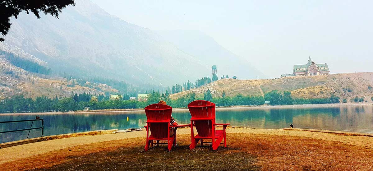 Red chairs on the beach looking towards Waterton Lake